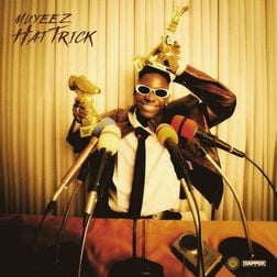 The cover art for "Hat Trick" by Muyeez features the artist standing triumphantly in front of a curtain backdrop. He is holding multiple trophies, including a golden shoe trophy, with a wide, celebratory smile. Muyeez is dressed in a suit, wearing sunglasses, and surrounded by several microphones, as if at a press conference. The title "HAT TRICK" is written in an elegant, handwritten-style font in the top left corner. The overall color scheme is warm, with golden and brown tones, giving the image a vintage, celebratory feel.